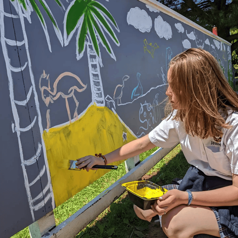 Girl artist painting a mural at school