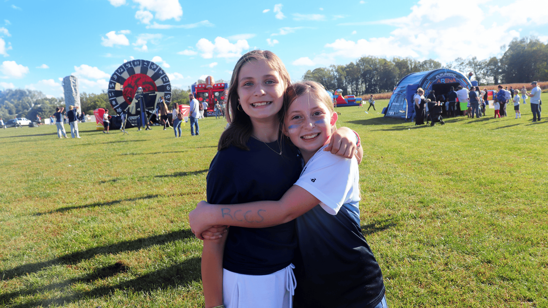 Private middle school girls enjoying the school fair, hugging with RCCS written on arms for school spirit